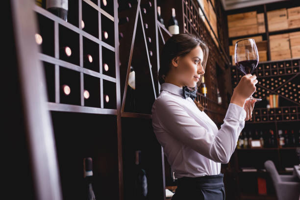 Selective focus of sommelier looking at wine in glass near racks with bottles Selective focus of sommelier looking at wine in glass near racks with bottles sommelier photos stock pictures, royalty-free photos & images