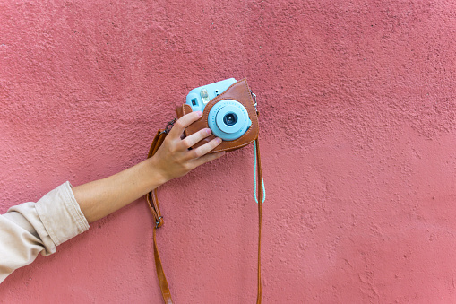 Woman arm holding a blue polaroid camera with a red wall on the background.