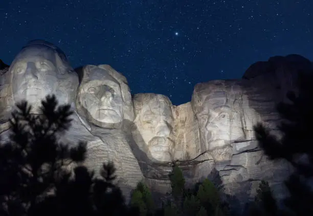 A view of Mount Rushmore in South Dakota at night with stars in sky and presidents illuminated.