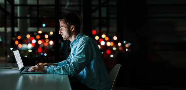 Working towards success through the night Shot of a businessman working on a laptop in an office at night working late photos stock pictures, royalty-free photos & images