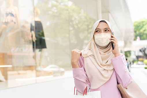 Portrait of a Muslim woman wearing a facemask while shopping and talking on the phone during the COVID-19 pandemic