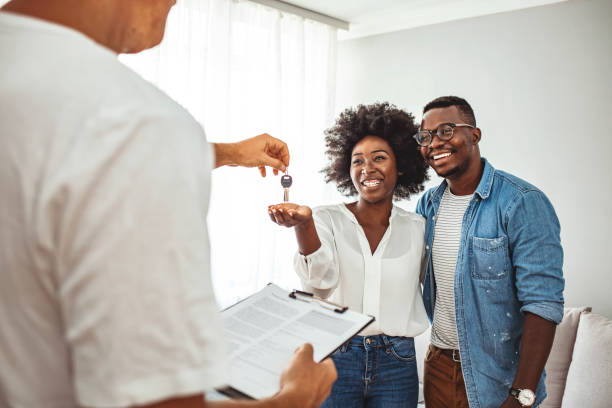 Handsome Real Estate Agent is giving key to the new apartment to happy young couple. Handsome Real Estate Agent is giving key to the new apartment to happy young couple. Couple buying new apartment. A young couple receive the keys to their new apartment from a letting agent. african american real estate agent stock pictures, royalty-free photos & images