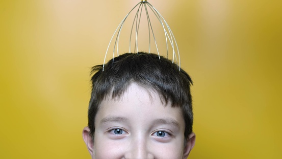 A caucasian boy enjoy head scalp massage by anti stress acupuncture metal octopus tool, equipment, she closes her eyes with pleasure, yellow background, close up view.