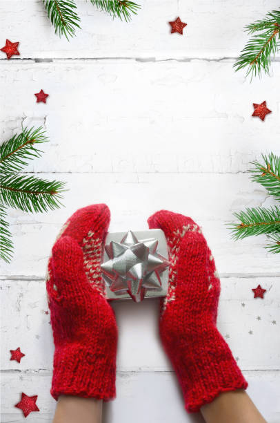 istock Hands in knitted mittens with gift box on white wooden table 1278107226