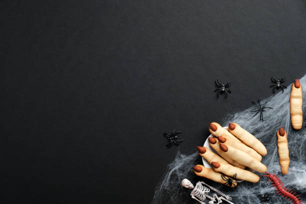 istock Halloween composition. Witch hand fingers, spiderweb, spiders, skeletons on black background. Flat lay, top view. Halloween pastry concept. 1278115630