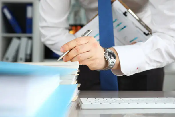 Photo of Man in tie makes notes on documents on table