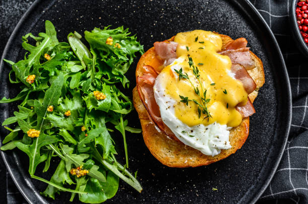 sanduíche de brioche com bacon, ovo benedict e molho hollandaise. enfeite com salada de rúcula. fundo preto. vista superior - hollandaise sauce fotos - fotografias e filmes do acervo