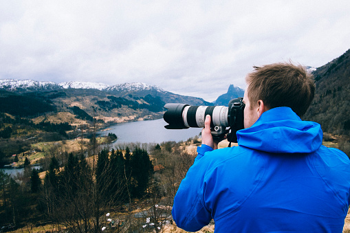 Nature and adventure photographer enjoying the view over Norwegian fjord with a telephoto lens on a DSLR camera.