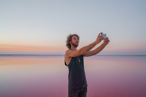 Young Caucasian man  taking picture on smartphone  on pink salt lake in Ukraine