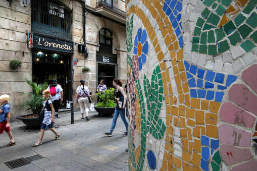 Barcelona, Spain - July 2, 2016: Close up of a pillar covered in Antonio Gaudi inspired mosaic in the Gothic quarter of Barcelona with people walking in the background.