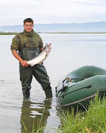 Khabarovsk region, Russia - August 16, 2020: Fisherman demonstrating fresh coho salmon ( Oncorhynchus kisutch ) catch  in his hands. Sea of Okhotsk coast. Khabarovsk region, far East, Russia.