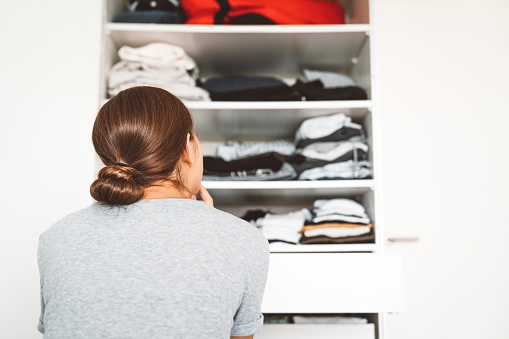 View from the back, woman sitting on the edge of the bed looking at her closed, deciding what to wear.