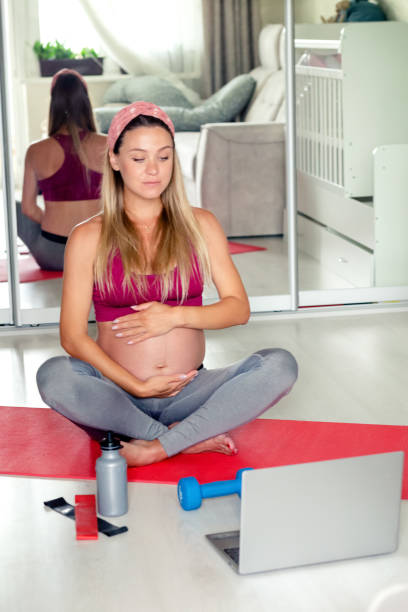 pregnant woman training yoga online at home stock photo