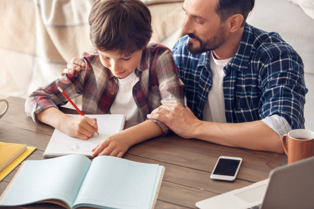 istock Father and son at home sitting at table dad hugging boy writing homework smiling happy close-up 1278157183