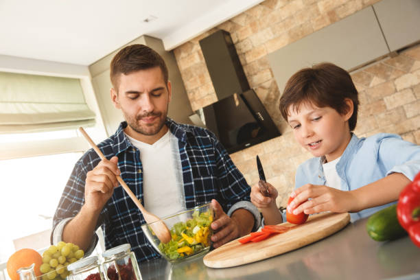 istock Family at home standing in kitchen together son cutting tomato on board while father mixing salad concentrated 1278157241