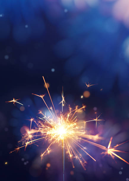 Glittering burning sparkler against fireworks background with copy space Glittering burning sparkler against fireworks background with copy space glittering burning stock pictures, royalty-free photos & images