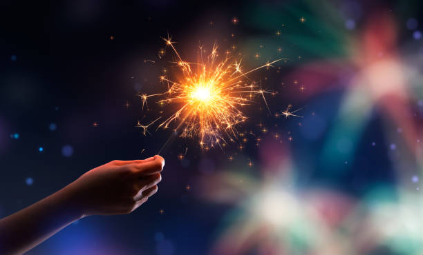 istock Hand holding a burning sparkler against fireworks background 1278170174