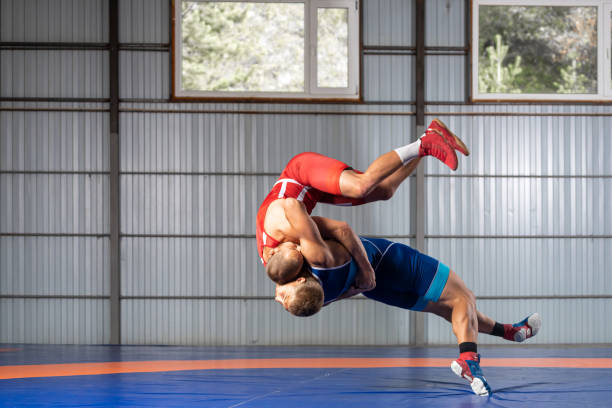 Two strong wrestlers Two strong wrestlers in blue and red wrestling tights are wrestlng  on a blue carpet in the gym. Young man doing grapple. wrestling stock pictures, royalty-free photos & images