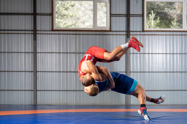 Two strong wrestlers Two strong wrestlers in blue and red wrestling tights are wrestlng on a blue carpet in the gym. Young man doing grapple. wrestling sport stock pictures, royalty-free photos & images