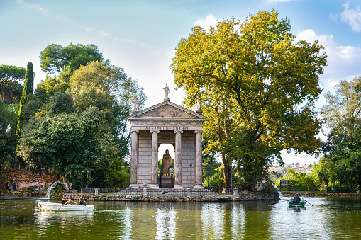 Rome, Italy, September 29 -- A peaceful view of the Villa Borghese lake, the green heart of Rome where citizens and tourists come to spend hours of relaxation and silence among avenues, littles lakes and gardens immersed in the green of ancient trees. In the background, the temple dedicated to the god of medicine Aesculapius, built in 1785 in the neoclassical style by the architects Antonio and Mario Asprucci. Image in High Definition format.