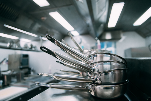 Stacks of metal frying pans on a counter in a professional kitchen\nBlurred background