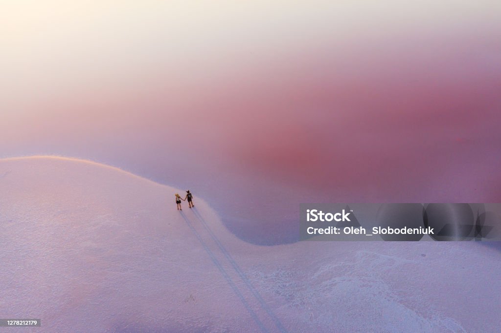 Scenic aerial view of couple walking on  pink salt lake Nature Stock Photo