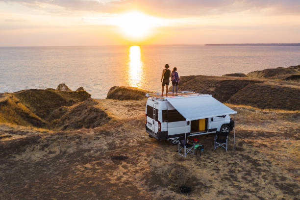 Aerial view of heterosexual couple on roof of camper van on seaside  at sunset Aerial view of the heterosexual couple on the roof of camper van on seaside  at sunset motor home photos stock pictures, royalty-free photos & images