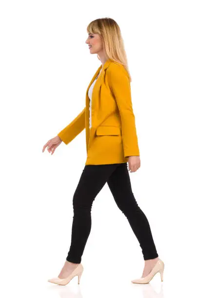 Photo of Young Woman In Yellow Jacket And High Heels Is Walking. Side View.