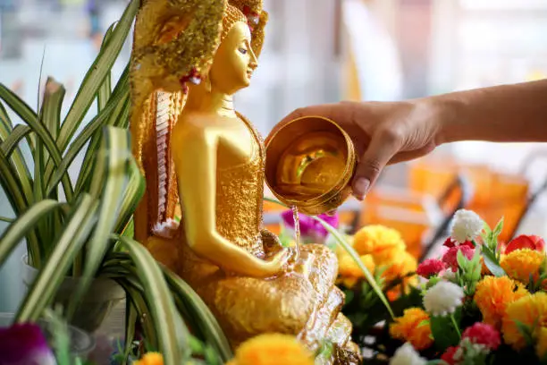 Close up hand of woman sprinkle water onto a gold Buddha image on Songkran Festival Day at Thailand.