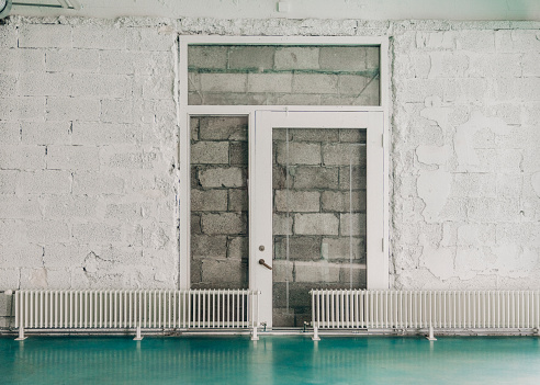 Radiators against white wall at entrance hall. Glass door is against concrete blocks.