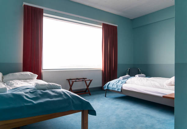Rolled towels on white twin double beds. Furniture in bright hostel bedroom. Interior of college dorm.