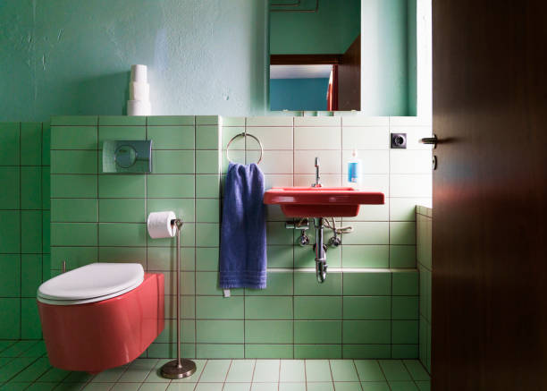 Toilet bowl by sink mounted on green tiled wall