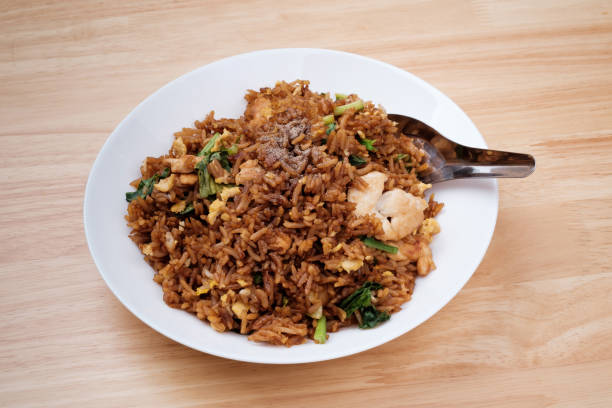 istock Thai style dark brown soy sauce fried rice with chicken, kale, and egg in white dish with short spoon on light wooden table 1278229012