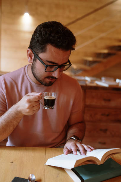 istock Young man drinking coffee in a cafeteria and reading a book 1278230563
