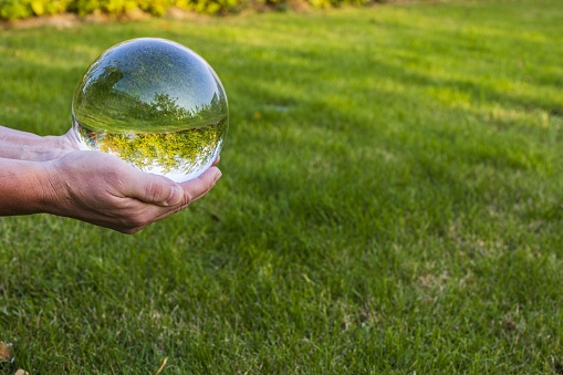 Close up macro view of hand holding crystal ball with inverted image of green natural landscape.