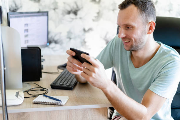 istock a young man sits at a computer table and plays a game on a smartphone 1278234128