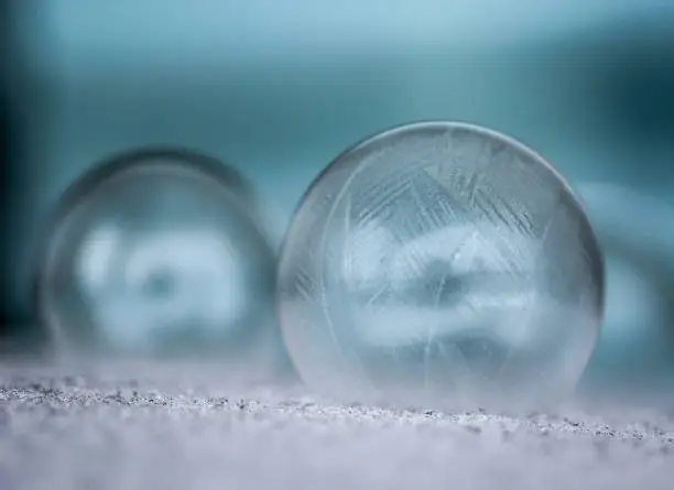Two frozen soap bubbles sitting on snow with soft blue background