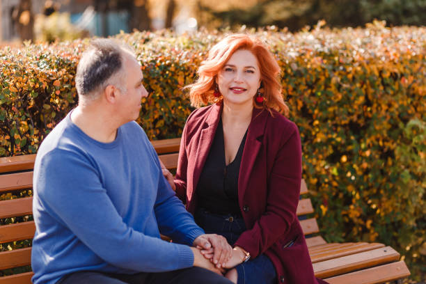 istock A smiling middle-aged woman and a man hold hands while sitting on a park bench in the fall. 1278240552