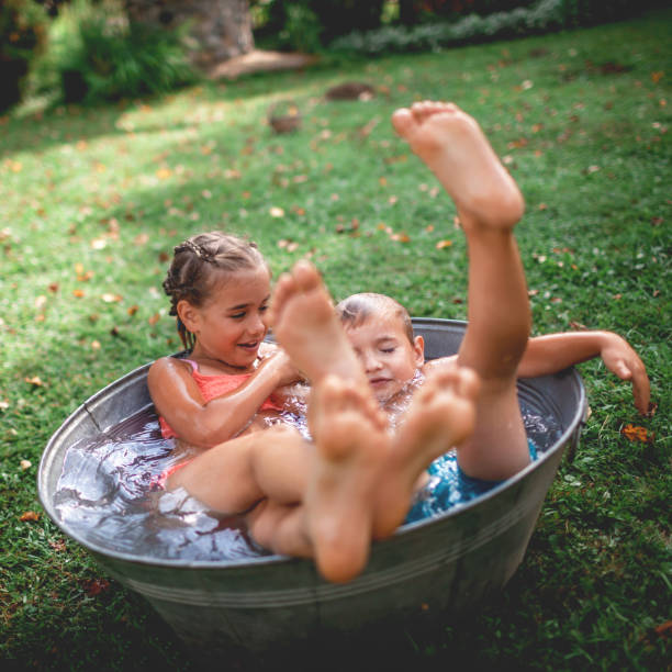 Summer vacation in countryside. Kids bathing and splashing in old bowl outdoor Summer vacation in countryside, local staycation. Cute kids having fun, bathing and splashing in old iron bowl on the backyard of wooden house, happy summertime, outdoor lifestyle, selective focus staycation photos stock pictures, royalty-free photos & images