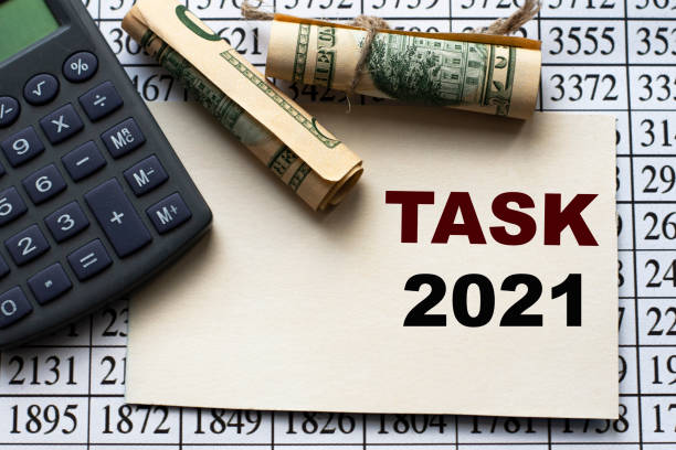 istock TASK 2021 word on a white sheet against a table with numbers, banknotes and calculator 1278240886