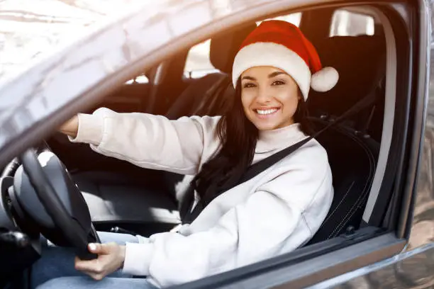 Happy New Year and Merry Christmas! A woman is sitting in a car, she is wearing a red santaclaus hat and smiling.
