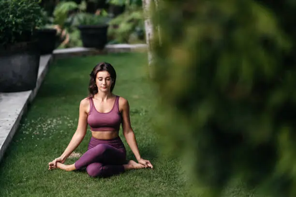 Woman practicing yoga performing yoga-asanas outdoors. Young attractive slim fitness girl in bodysuit relaxing and doing exercises.