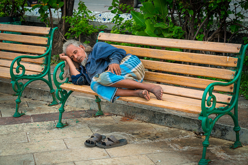 Bandra, Mumbai / India - 3rd October 2020 - Atired fisherman or a poorman sleeps peacefully on a bench by the sea