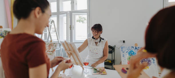 Mature woman painting in art class Photo of a smiling mature woman taking painting classes with her friends in a local art studio; connecting with her friends over a glass of wine and learning how to paint together. 55 59 years photos stock pictures, royalty-free photos & images
