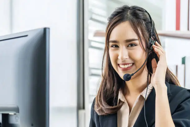 Smiling friendly asian female call-center agent with headset working on support hotline in the office