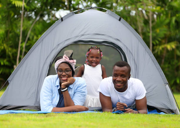 famille afro-américaine heureuse passant du temps ensemble pendant des vacances sur le parc extérieur de tente de camping - camping family tent couple photos et images de collection