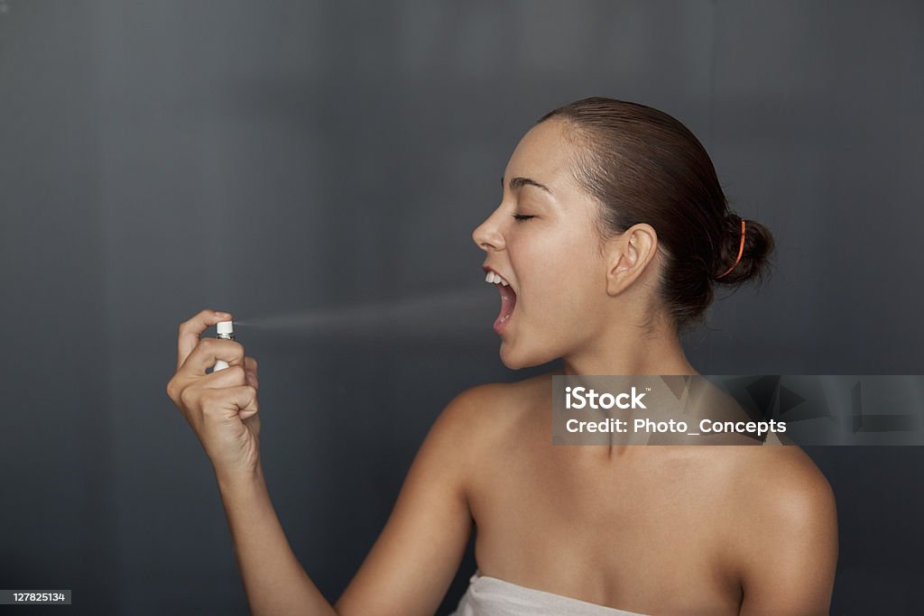 Mujer pulverización de aerosol de aire en la boca - Foto de stock de Atomizador bucal libre de derechos