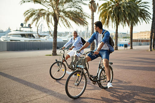 Carefree mixed race male family members in early 20s and late 40s enjoying cycling while vacationing in Barcelona.