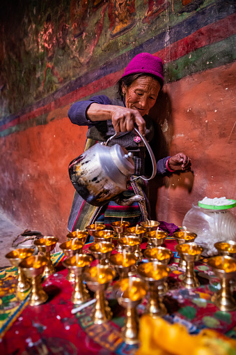 Old Tibetan woman lighting candles in monastery in small village near Lo Manthang, Upper Mustang. Mustang region is the former Kingdom of Lo and now part of Nepal,  in the north-central part of that country, bordering the People's Republic of China on the Tibetan plateau between the Nepalese provinces of Dolpo and Manang.