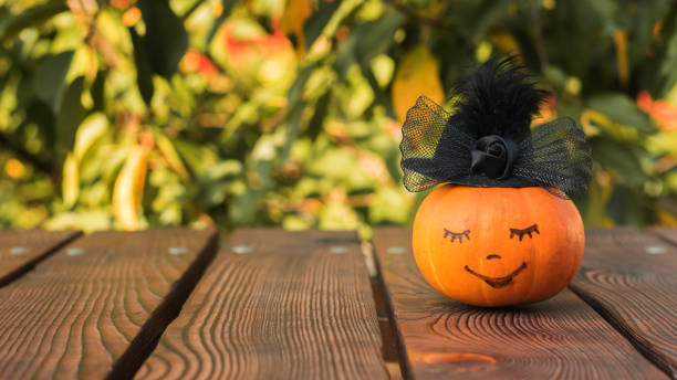istock Pumpkin with a smiling face in a black hat on a wooden table. 1278255337